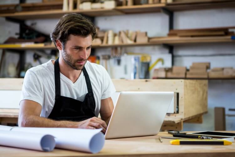 Artisan du BTP utilisant un ordinateur portable dans son atelier pour préparer ses factures électroniques